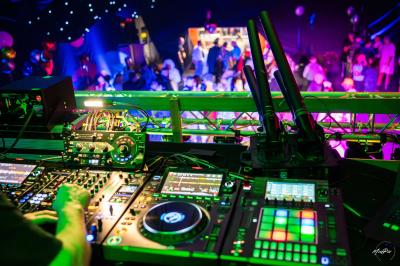 Vue depuis une table de mixage sur une salle éclairée par des lumières colorées, avec des invités assis et debout.