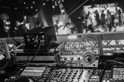 Vue depuis une table de mixage sur une salle éclairée par des lumières colorées, avec des invités assis et debout.