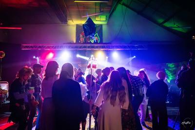 Vue depuis une table de mixage sur une salle éclairée par des lumières colorées, avec des invités assis et debout.