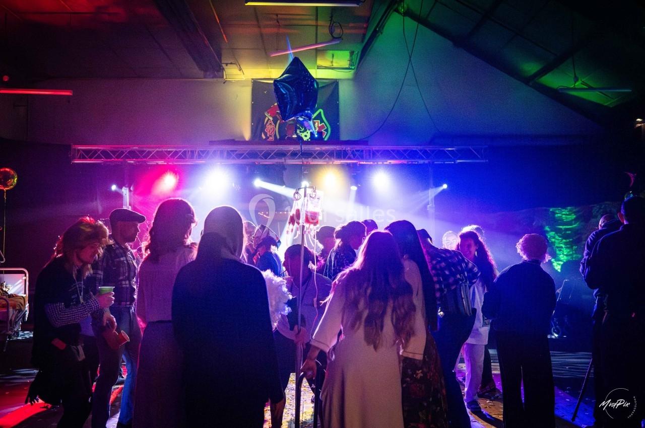 Groupe de personnes dansant sous des lumières colorées dans une salle sombre lors d'un événement festif.