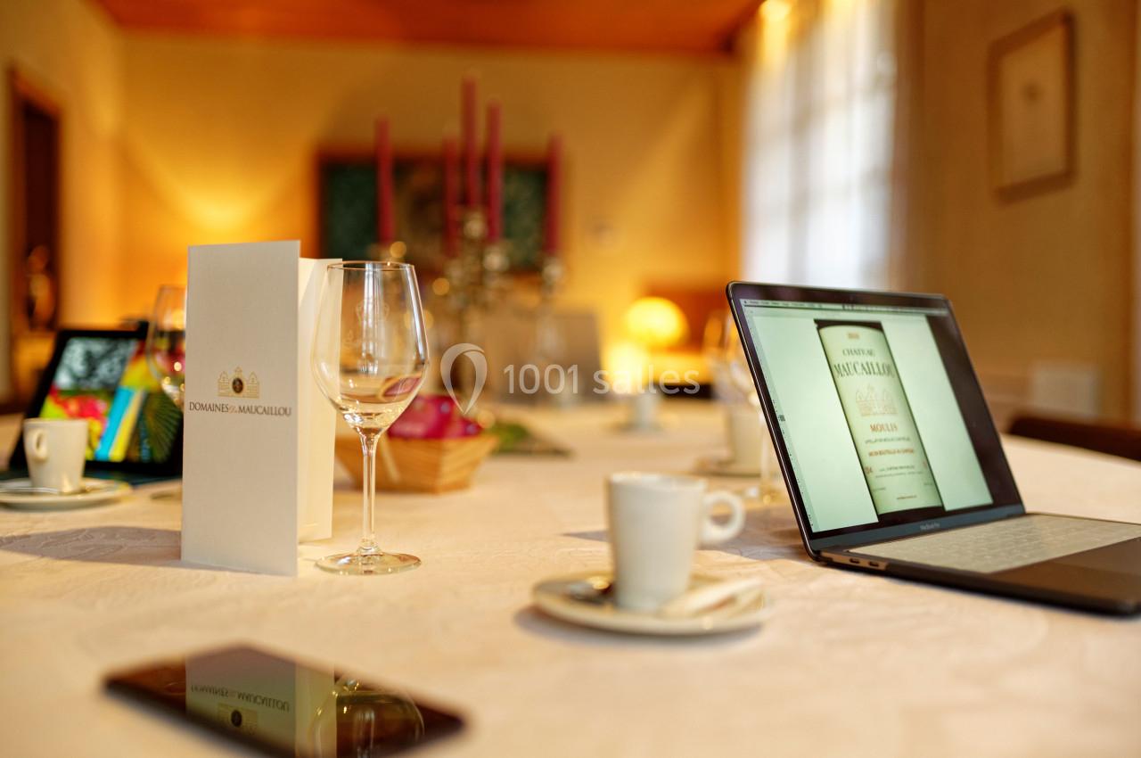 Table dressée avec des verres, tasses à café, un menu, un ordinateur portable ouvert et des chandeliers en arrière-plan.