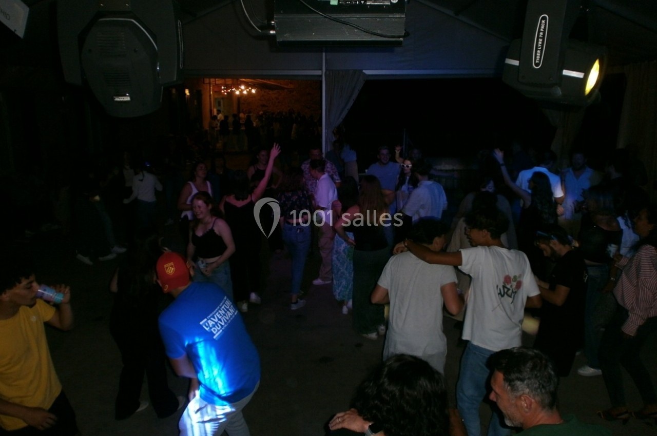 Groupe de personnes dansant et discutant dans un espace sombre éclairé par des lumières artificielles.