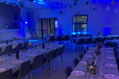 Salle décorée pour un événement, avec tables dressées, ballons suspendus et éclairage bleu tamisé.