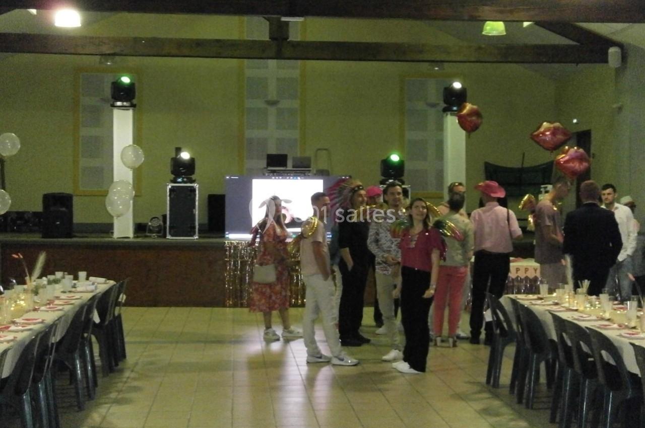 Des personnes déguisées discutent dans une salle décorée pour une fête, avec tables dressées et scène en arrière-plan.