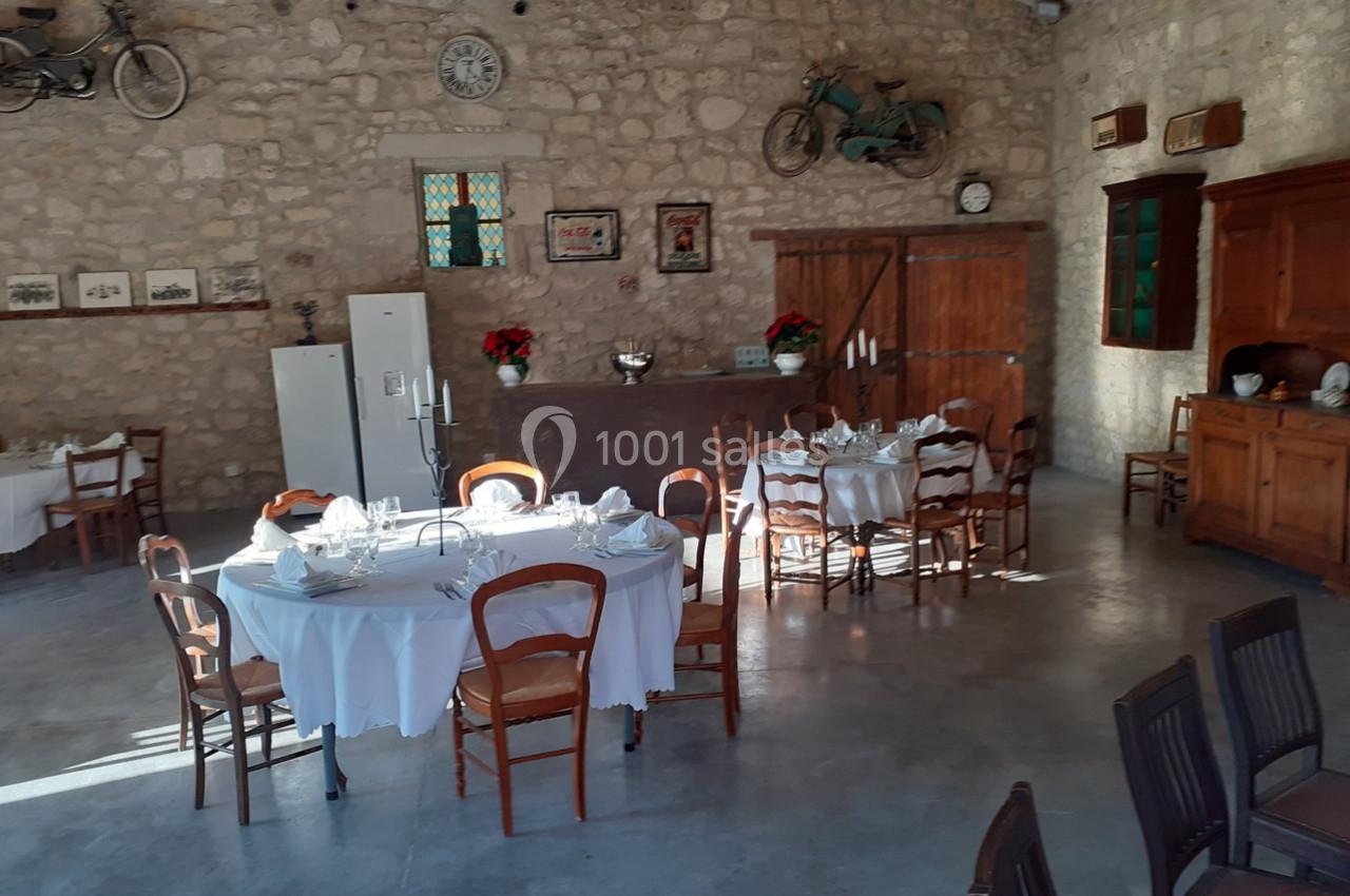 Salle en pierre avec tables rondes dressées, chaises en bois, décorations murales rétro et lumière naturelle.