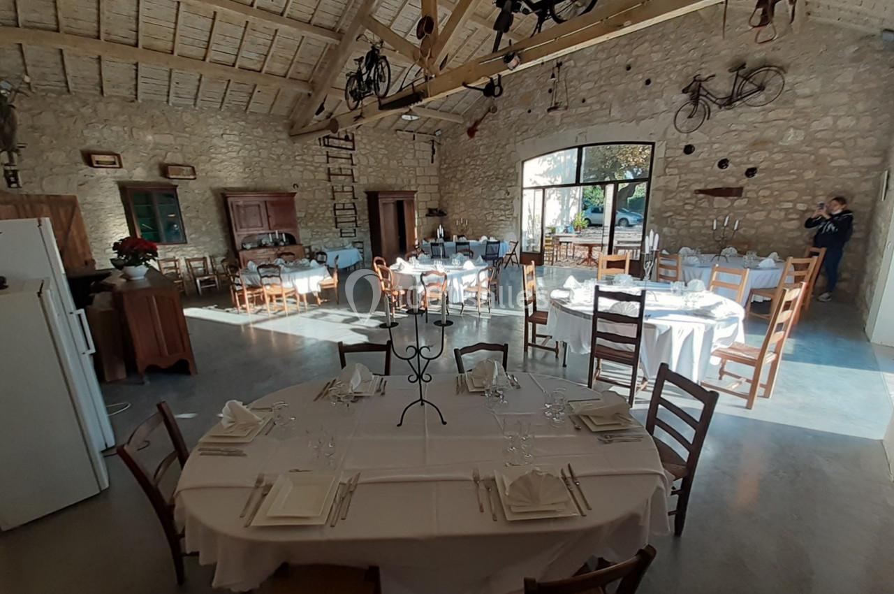 Salle lumineuse avec murs en pierre, tables rondes dressées pour un repas, et décoration rustique avec vélos suspendus.