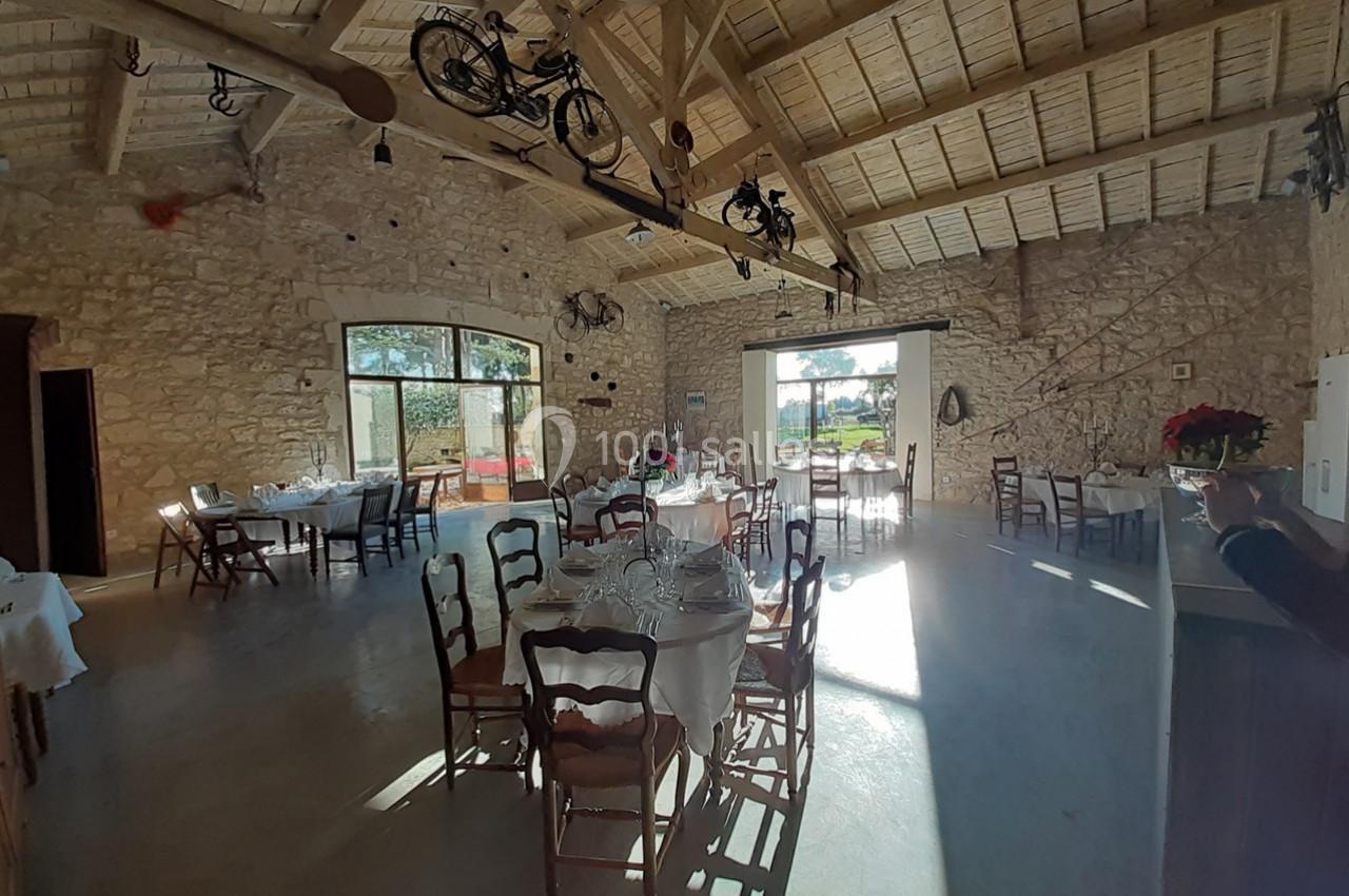 Salle lumineuse avec murs en pierre, tables dressées, poutres apparentes et vélos suspendus au plafond.