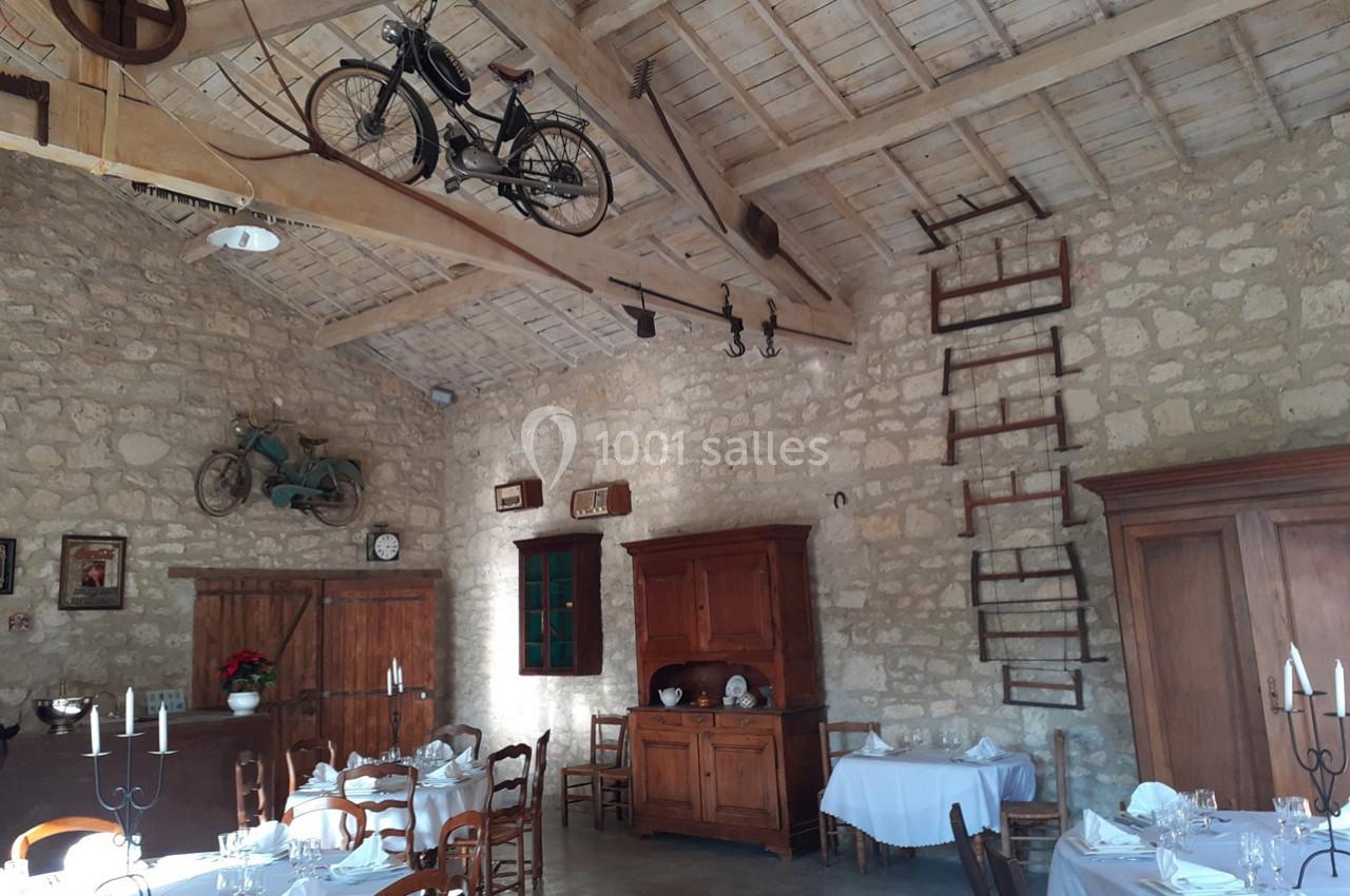 Salle de restaurant rustique avec murs en pierre, meubles en bois, tables dressées et vélos suspendus au plafond.