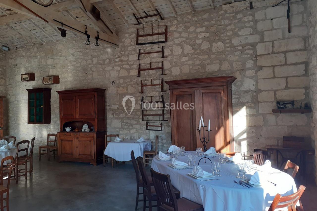 Salle à manger rustique avec murs en pierre, meubles en bois, tables dressées et lumière naturelle.