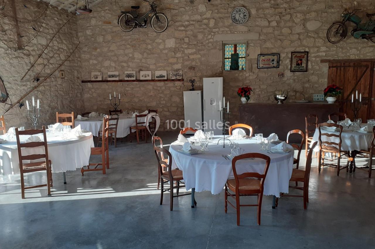 Salle de réception rustique avec murs en pierre, tables rondes dressées et décorations murales vintage.