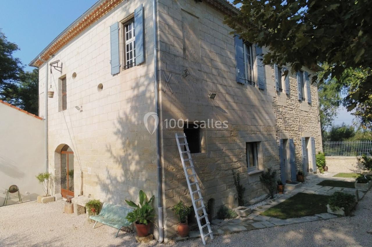 Façade d'une maison en pierre avec volets bleus, échelle appuyée et jardin aménagé autour.