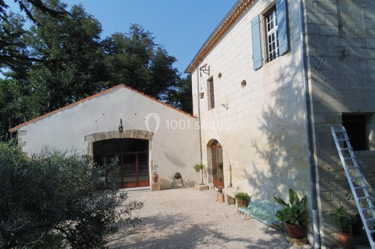 Cour extérieure avec façade en pierre, fenêtres à volets bleus, végétation et échelle appuyée contre le mur.