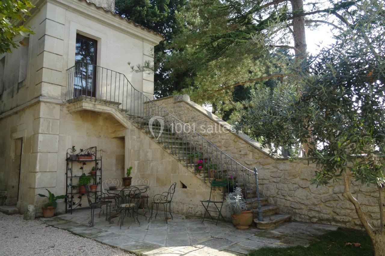 Escalier extérieur en pierre menant à une porte, avec terrasse aménagée de mobilier en fer forgé et plantes en pot.