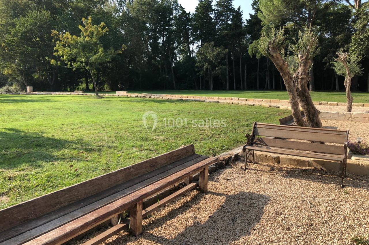 Bancs en bois et allée gravillonnée bordant une pelouse verdoyante, avec des arbres en arrière-plan.