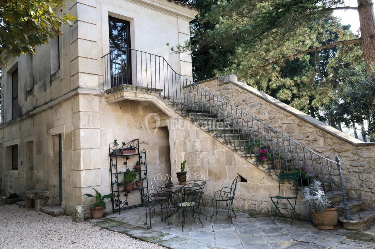 Escalier en pierre menant à une maison ancienne avec terrasse aménagée de tables, chaises et plantes en pots.