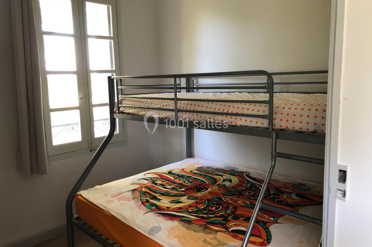 Lit superposé en métal dans une petite chambre lumineuse avec une fenêtre et des draps colorés.