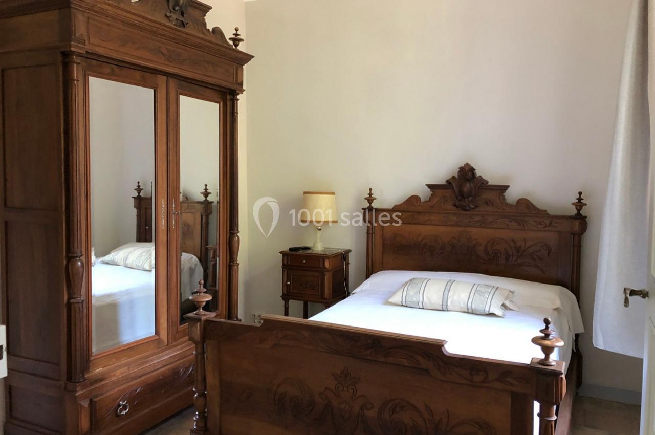 Chambre avec lit double en bois sculpté, armoire à miroir assortie, table de chevet et lampe dans un décor classique.