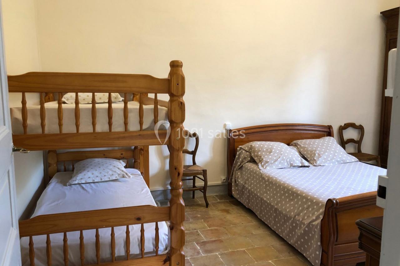 Chambre avec un lit double, des lits superposés en bois, une chaise et un sol en carrelage ancien.