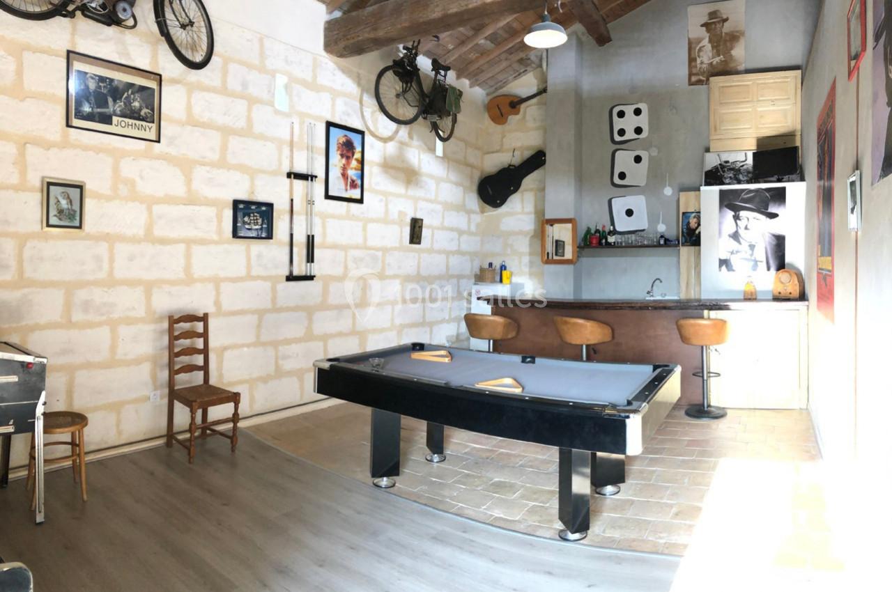 Salle de loisirs avec billard, bar, décorations murales variées et vélos suspendus sous un plafond en bois.