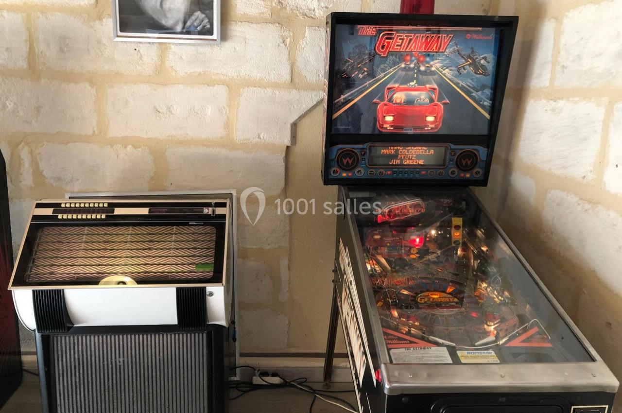 Un flipper et un jukebox vintage placés côte à côte dans une pièce aux murs en pierre.