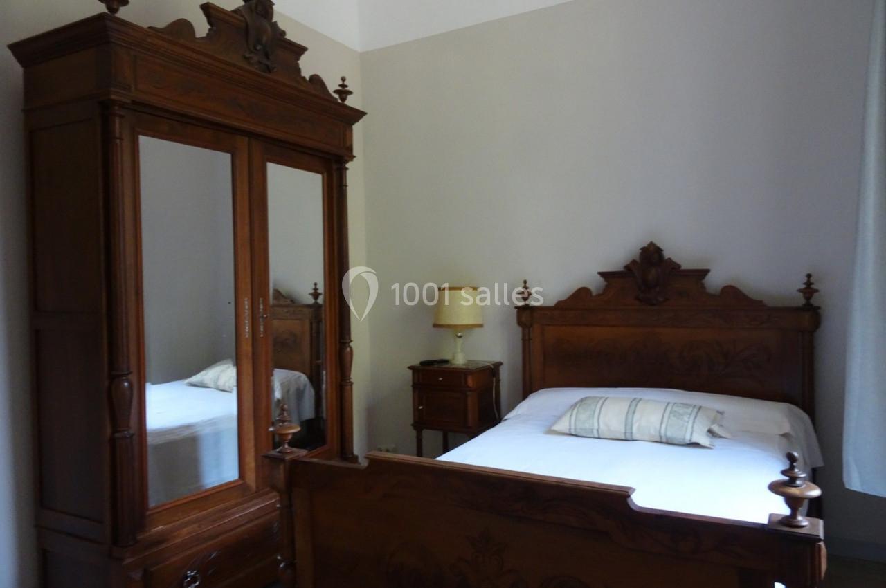 Chambre avec un lit en bois sculpté, une armoire assortie avec miroir et une lampe sur une table de chevet.