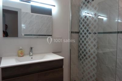 Salle de bain avec douche à l'italienne, lavabo double vasque, miroir éclairé et toilettes sur carrelage en terre cuite.