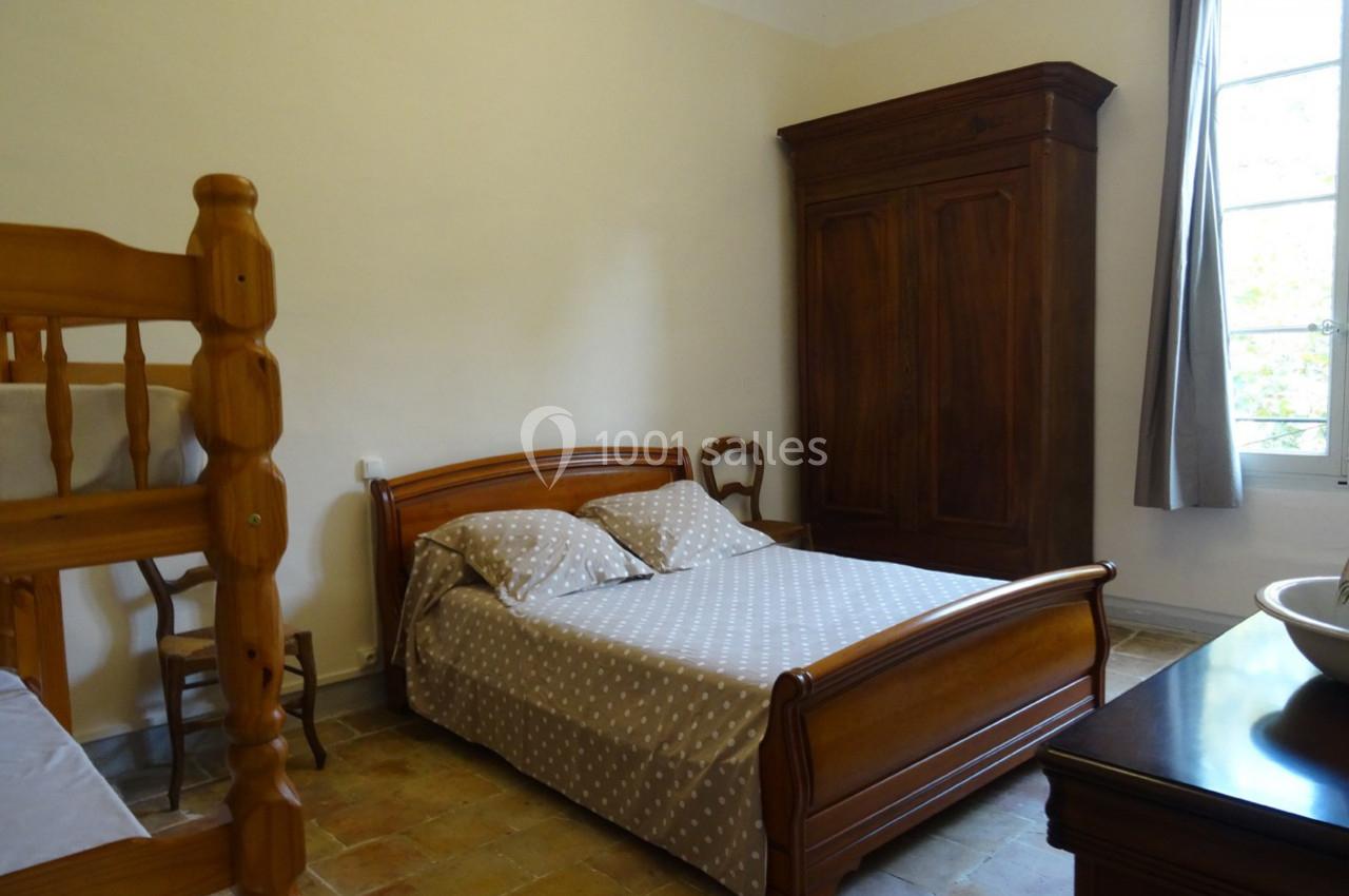 Chambre avec lit double, lits superposés en bois, armoire ancienne et fenêtre laissant entrer la lumière naturelle.