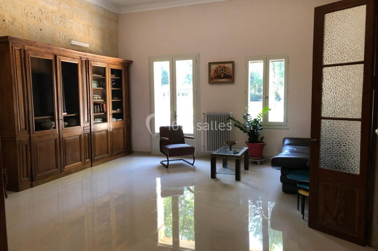 Salon lumineux avec sol en carrelage brillant, meubles en bois, fauteuils, table basse et plante près d'une fenêtre.