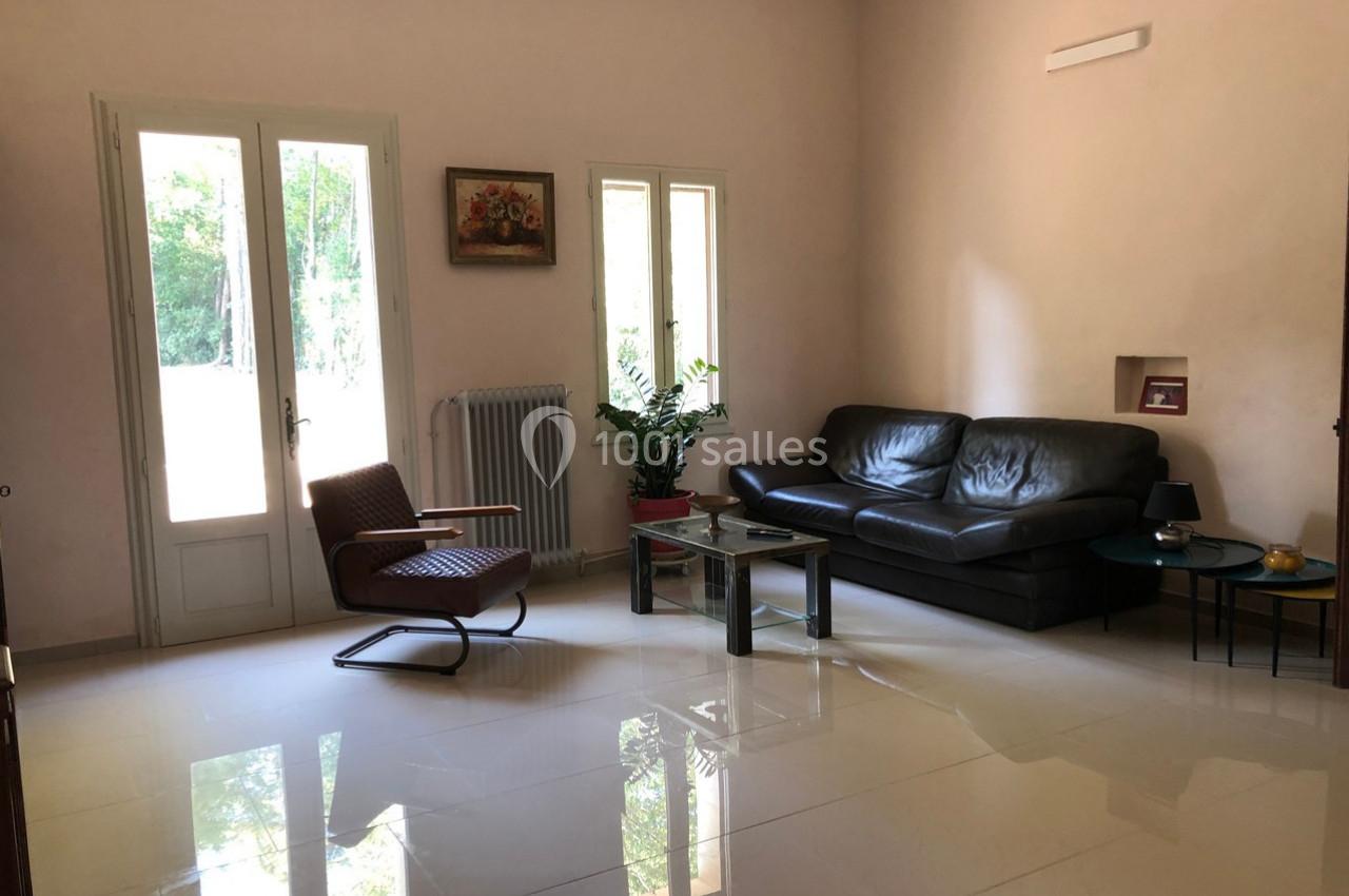 Salon lumineux avec canapé en cuir noir, fauteuil, table basse en verre et vue sur un jardin par une porte vitrée.