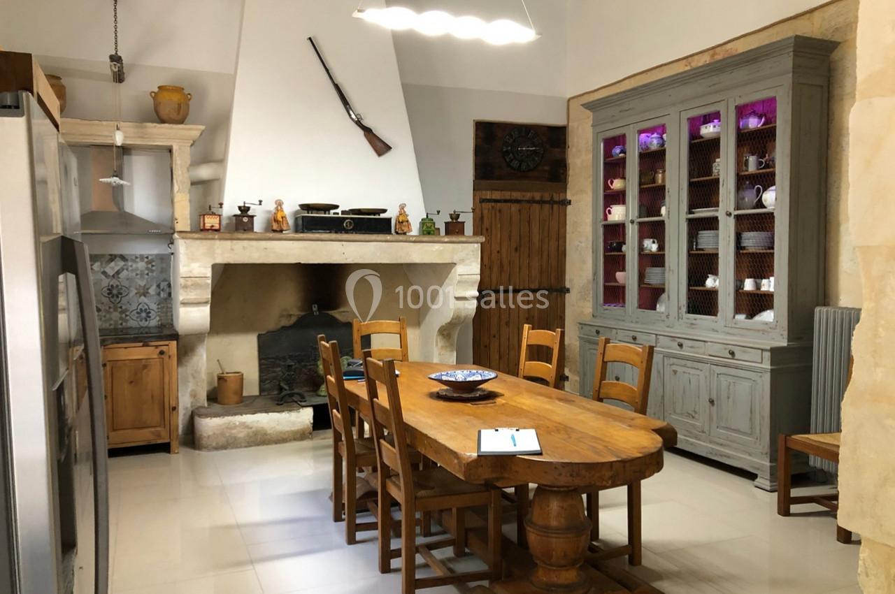 Cuisine rustique avec table en bois, cheminée en pierre, vaisselier gris et décoration murale traditionnelle.