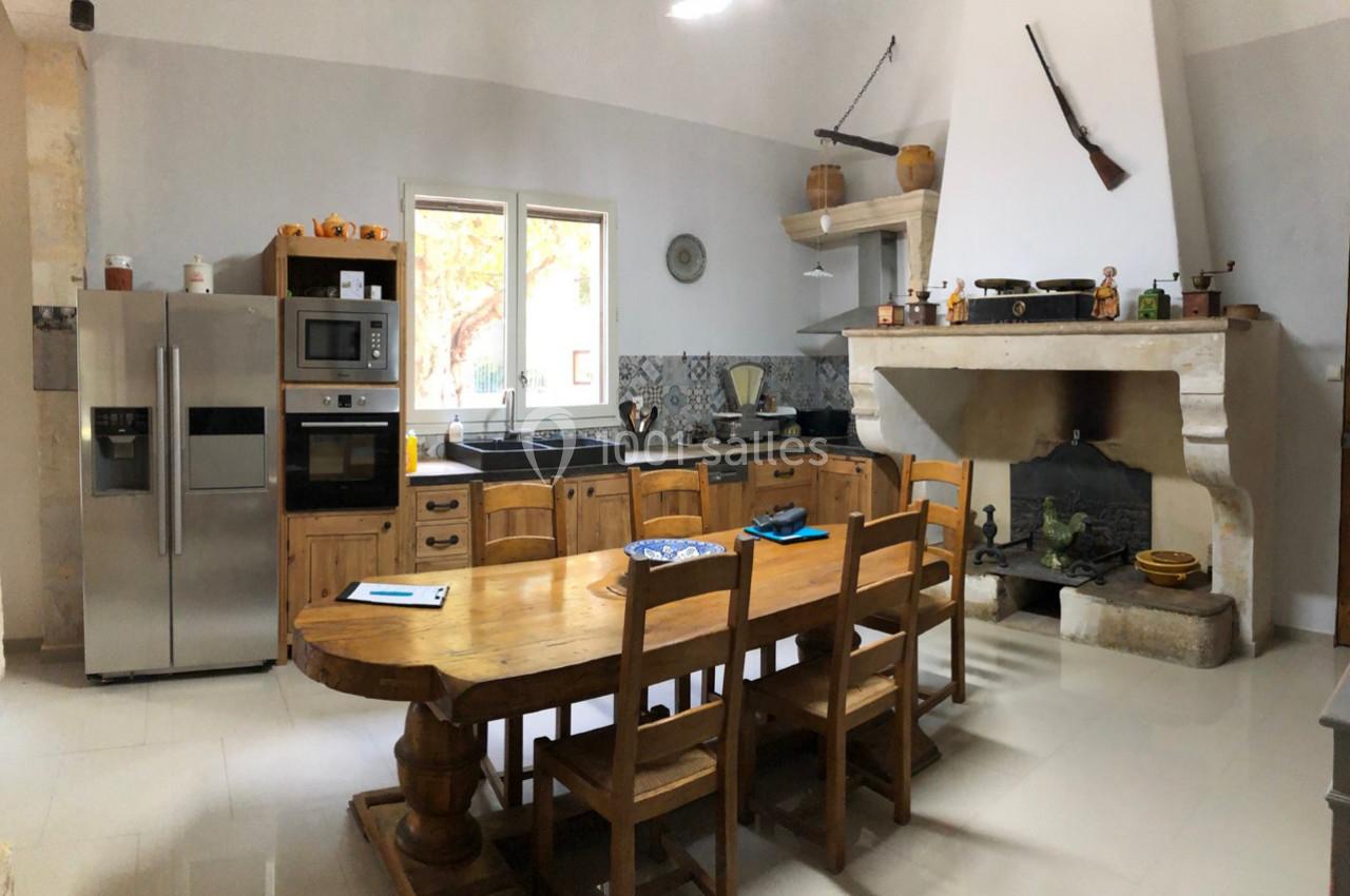 Cuisine rustique avec table en bois, cheminée ancienne, électroménagers modernes et fenêtres donnant sur l'extérieur.