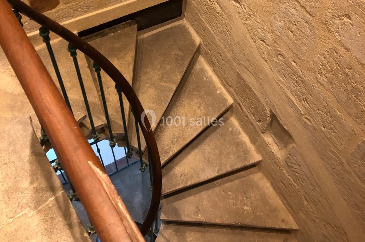 Escalier en colimaçon en pierre avec une rampe en bois, situé dans un bâtiment aux murs en pierre.