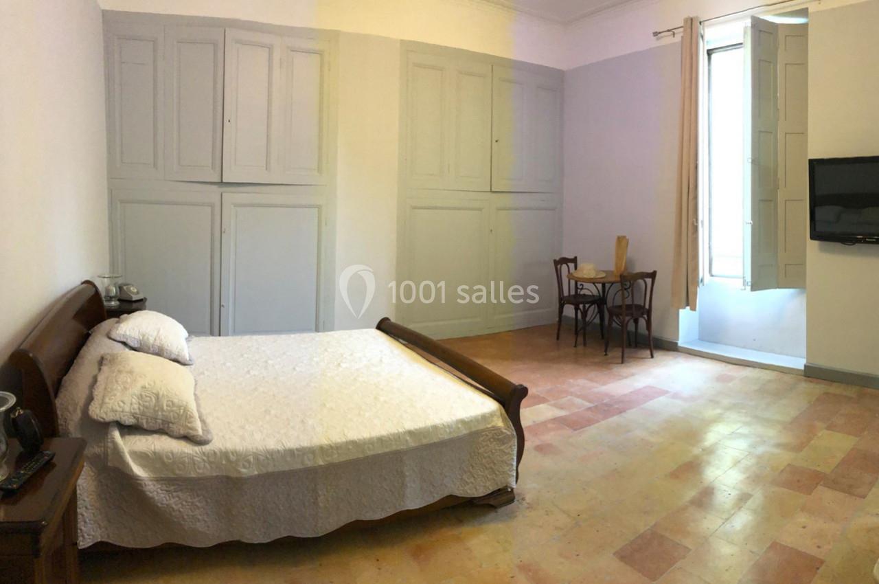 Chambre lumineuse avec lit double, table et chaises en bois, armoire murale et fenêtre ouverte sur le côté.