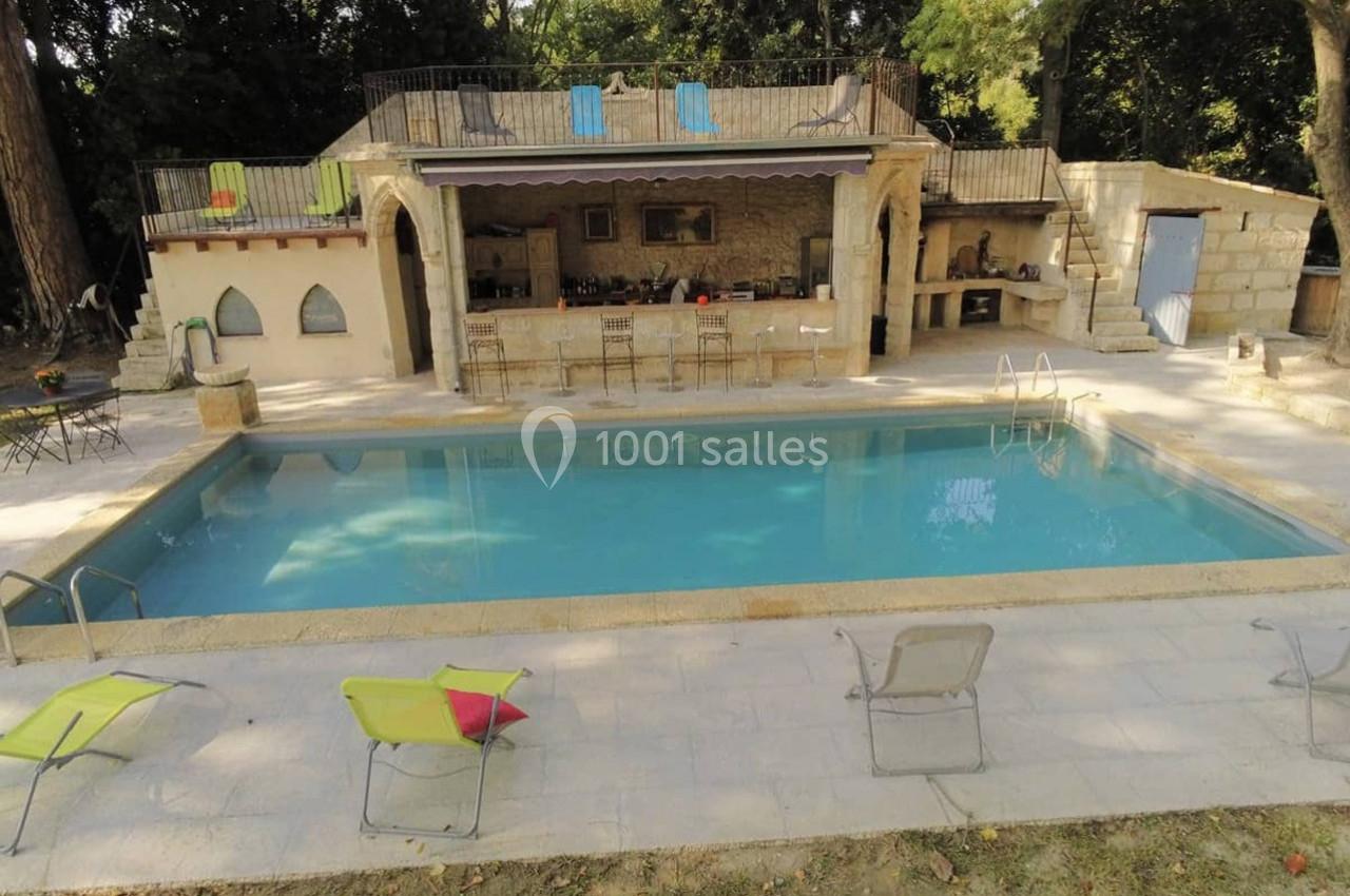 Piscine extérieure entourée de chaises longues, avec une terrasse en pierre et un espace cuisine en arrière-plan.