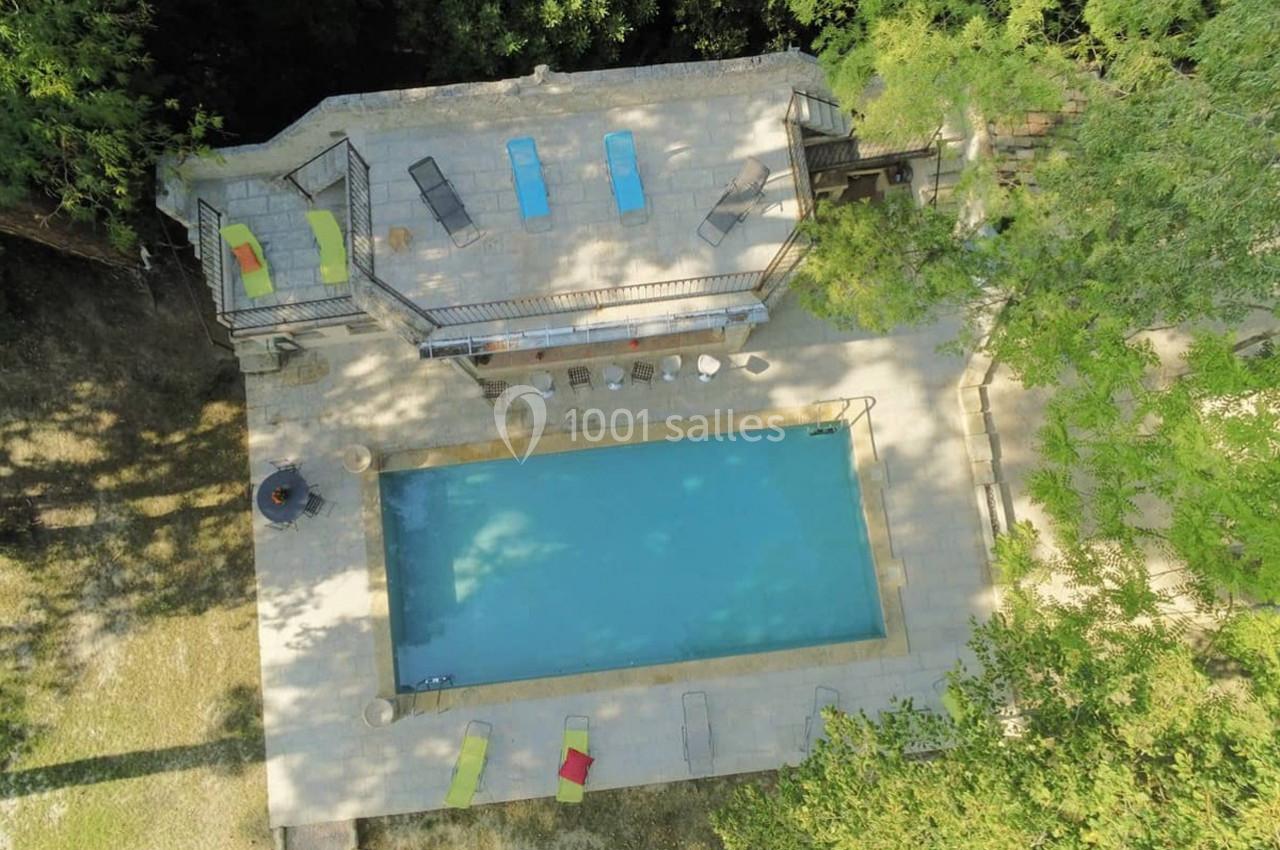 Vue aérienne d'une piscine rectangulaire entourée de transats et d'arbres, avec une terrasse en pierre.