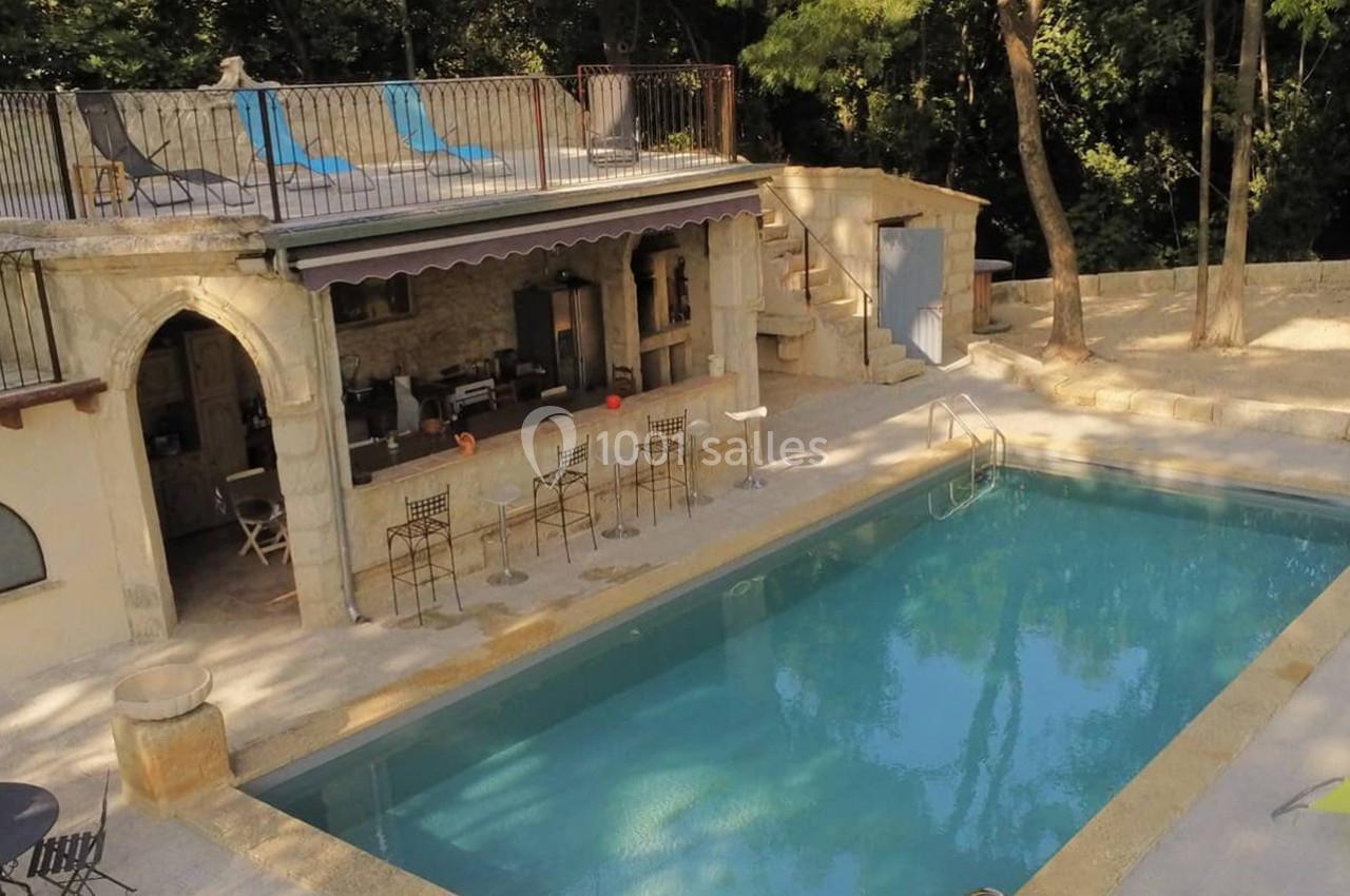 Piscine extérieure entourée de pierres, avec un pool house équipé de chaises hautes et d'une terrasse ombragée.