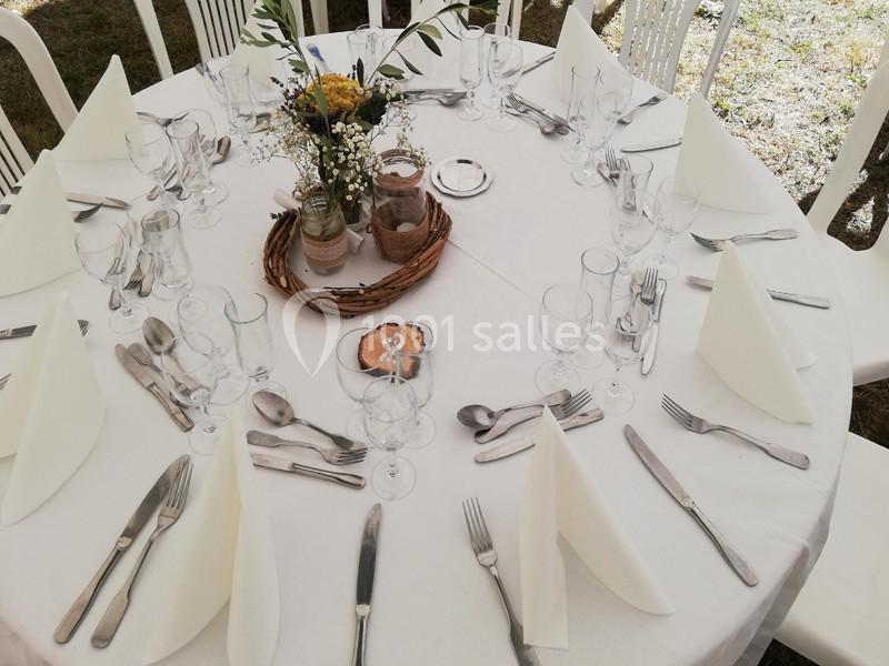 Table ronde dressée avec une nappe blanche, couverts, verres, serviettes pliées et centre de table floral.
