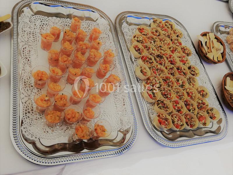 Plateaux de verrines de crevettes et bouchées garnies de légumes colorés, disposés sur des nappes blanches.