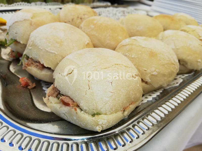 Plateau de petits sandwichs ronds garnis de légumes et de viande, disposés sur une nappe blanche.
