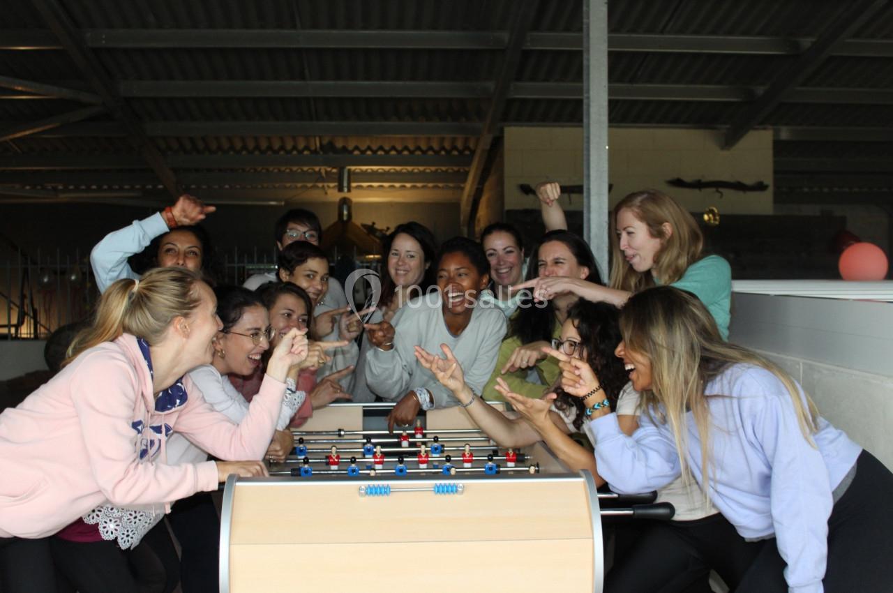 Des personnes souriantes jouent et s'amusent autour d'un baby-foot dans un espace intérieur.
