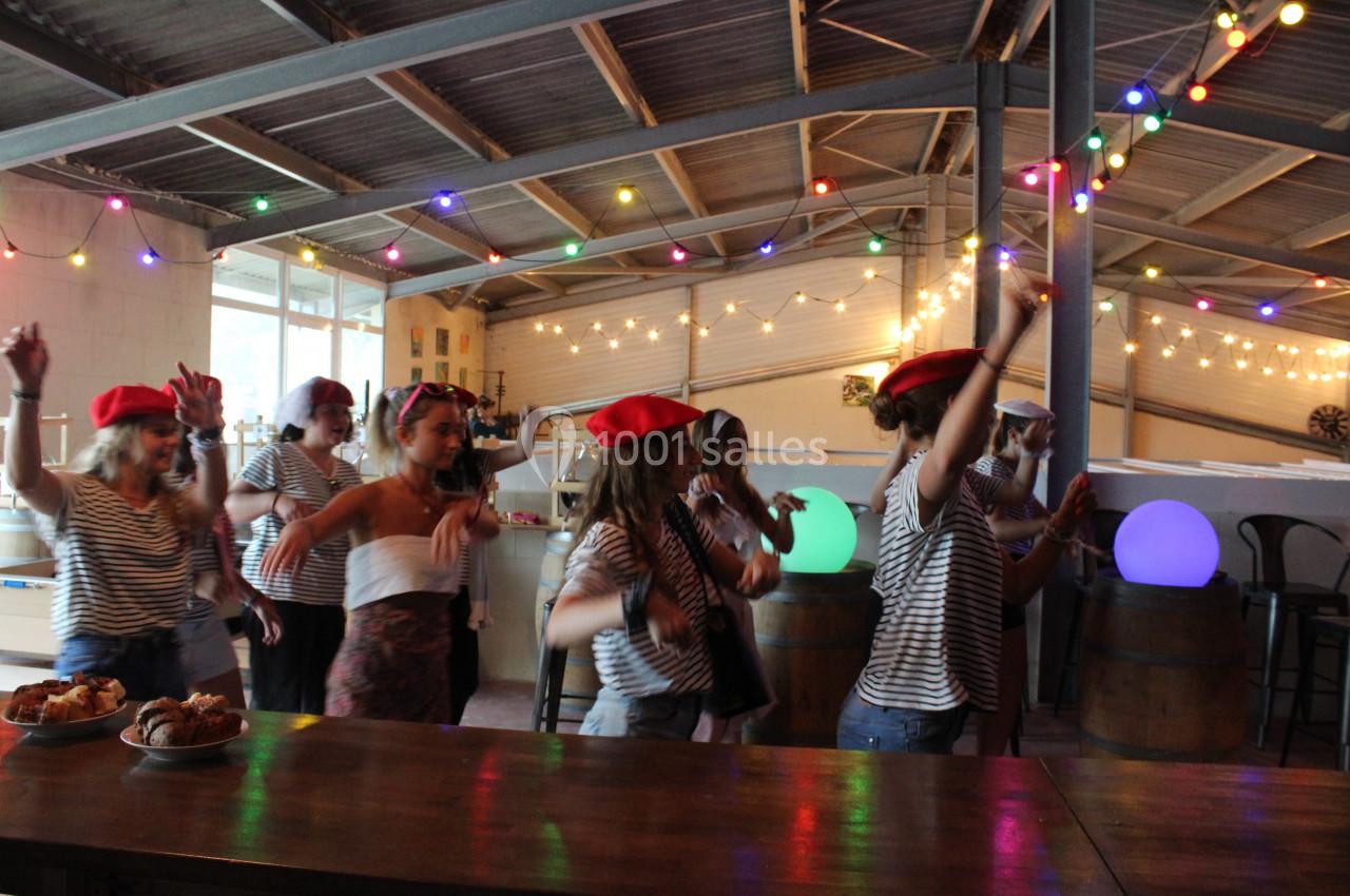 Des personnes en tenue marinière et béret rouge dansent dans un espace décoré de guirlandes lumineuses.
