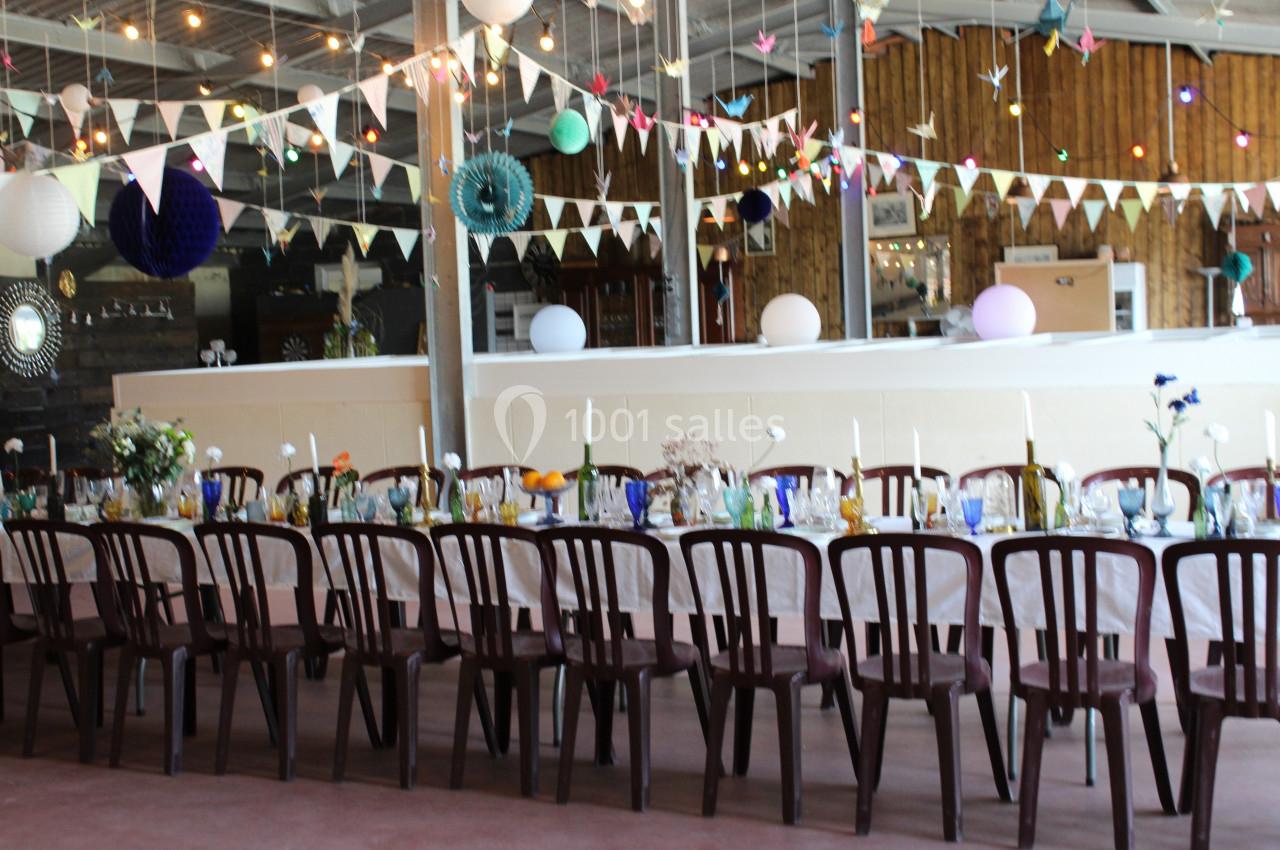 Salle décorée pour un événement avec une longue table dressée, des guirlandes lumineuses et des fanions suspendus.