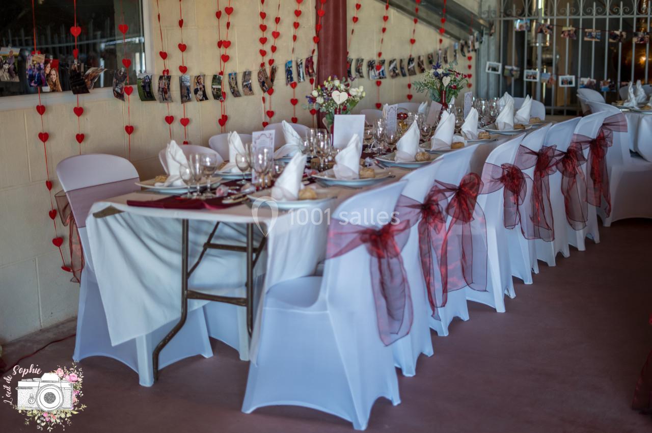 Table décorée pour un événement, avec nappes blanches, serviettes pliées, rubans rouges et guirlandes de cœurs en arrière…