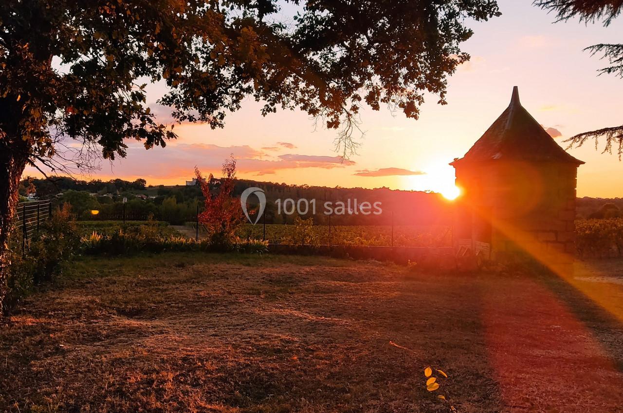 Coucher de soleil illuminant un jardin avec un petit bâtiment en pierre et des arbres en arrière-plan.