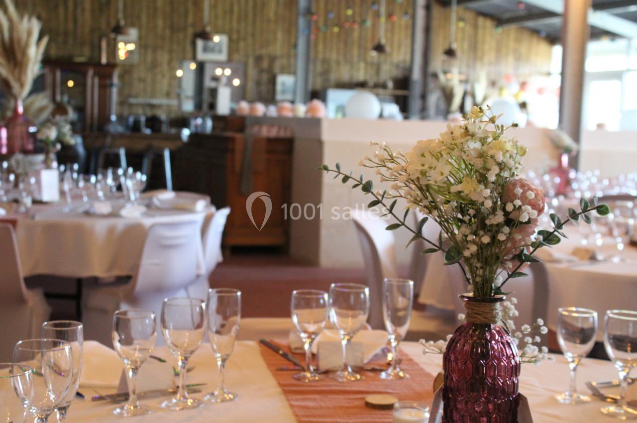 Salle de réception décorée avec des tables dressées, des fleurs en centre de table et une ambiance chaleureuse.