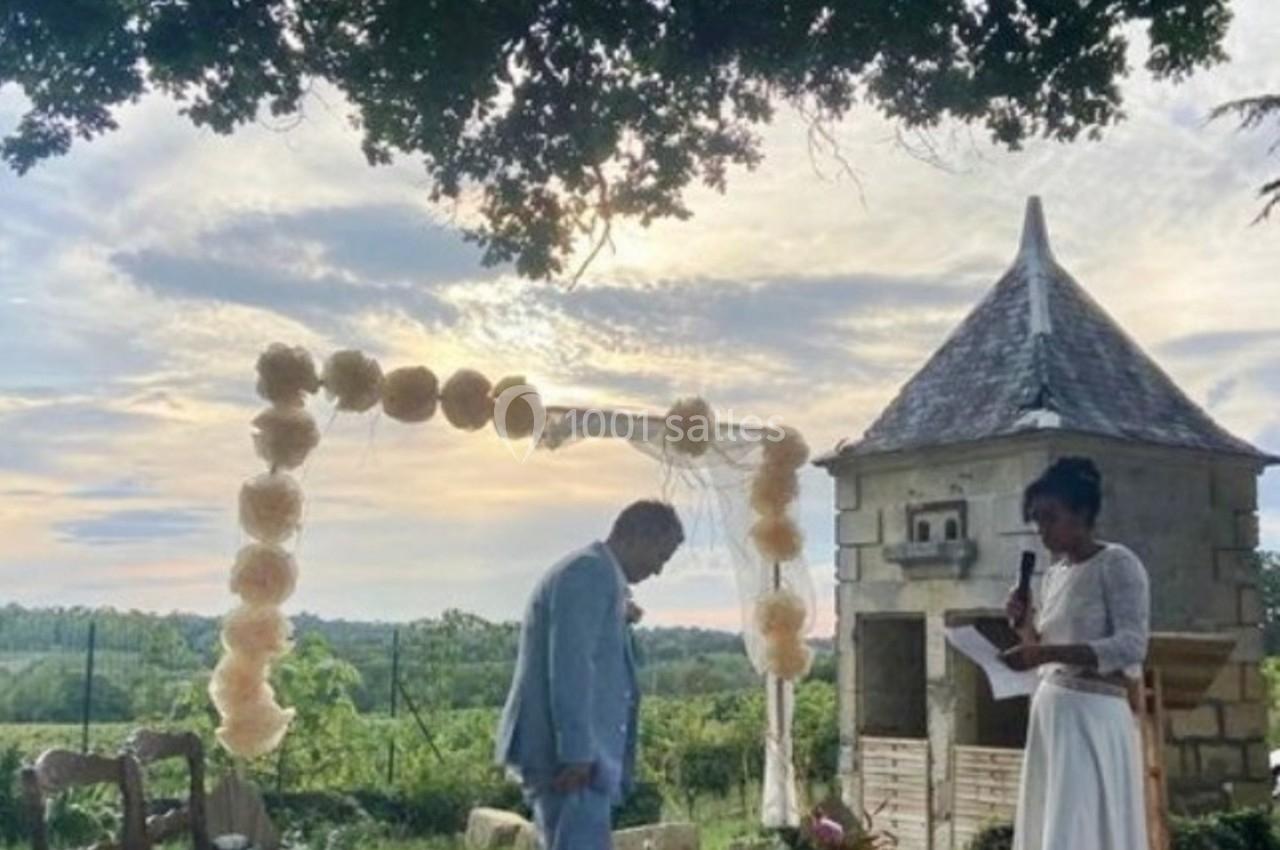 Un couple échange des vœux sous une arche décorée de fleurs dans un jardin au coucher du soleil.