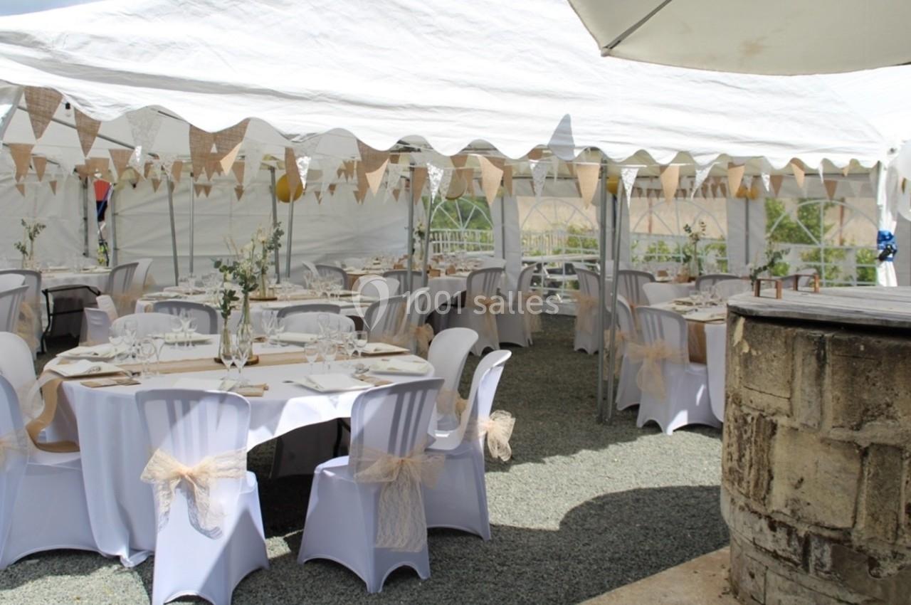 Tables décorées sous une tente blanche avec nappes, chaises ornées de rubans et guirlandes en toile de jute.