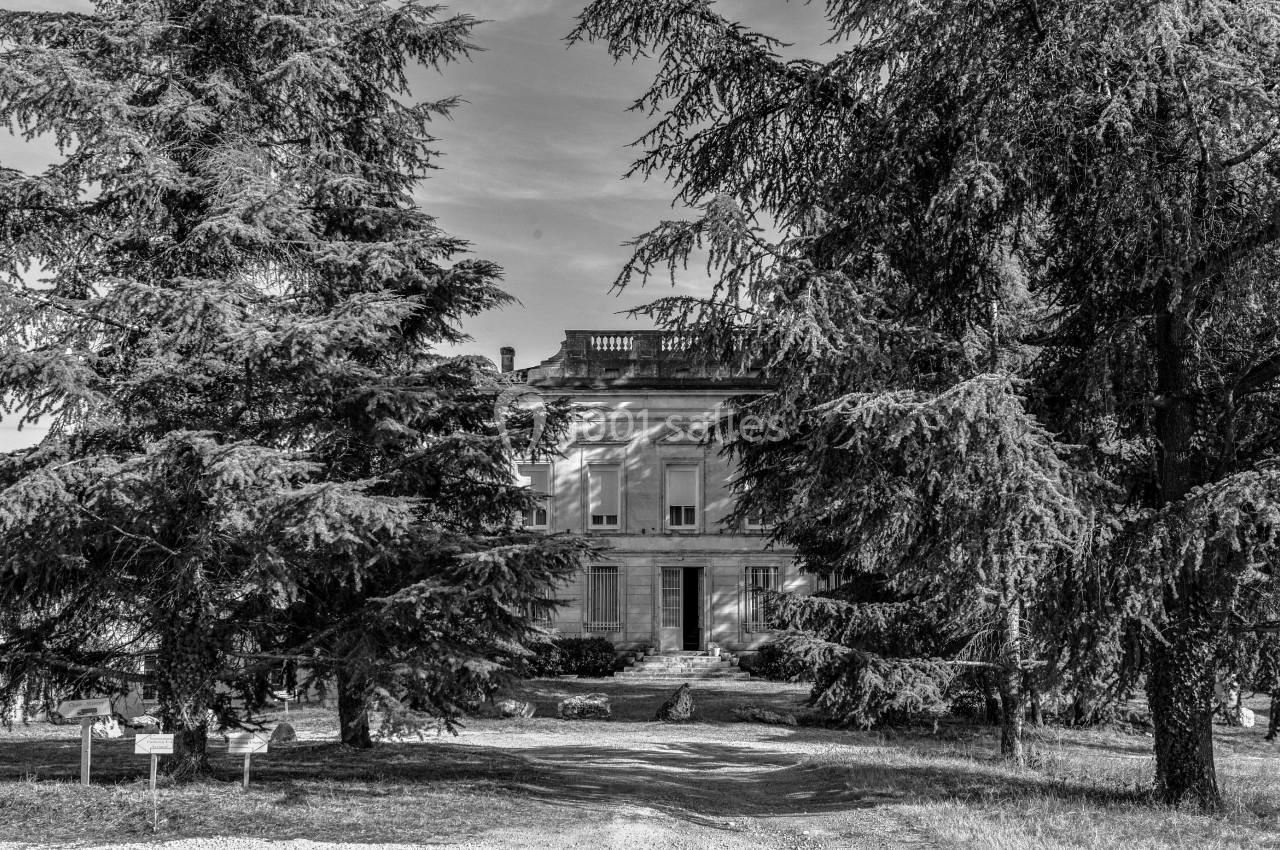 Façade d'un bâtiment ancien entouré de grands arbres, avec une allée menant à l'entrée principale.