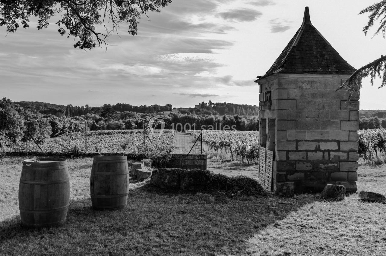 Vue en noir et blanc d'un paysage rural avec un petit bâtiment en pierre, des tonneaux et des vignobles à l'arrière-plan.