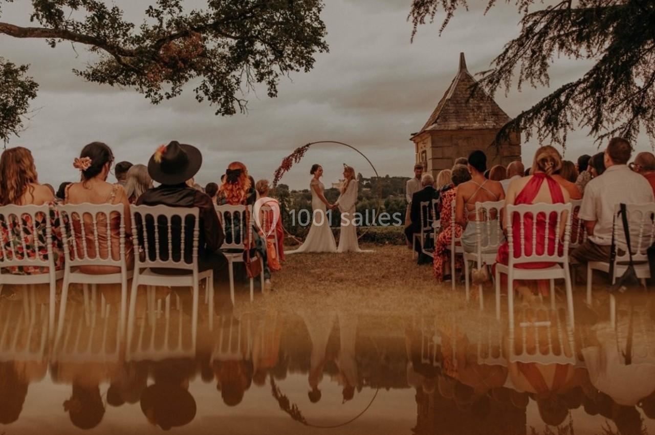 Deux personnes échangent leurs vœux lors d'une cérémonie en plein air, entourées d'invités assis, avec un paysage naturel en…